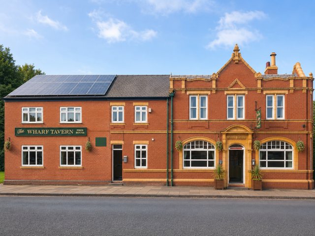 The front of The Wharf Tavern on Caroline Street, Stalybridge - a red brick free house with green painted windows and hanging baskets